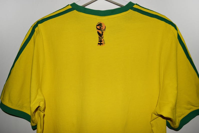 May include: Yellow short-sleeved t-shirt with green trim and a small graphic of a soccer trophy on the back.