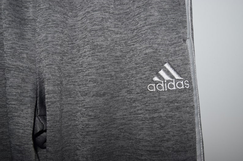 Puede incluir: Pantalones de ch&aacute;ndal grises con un logotipo de Adidas blanco en la pierna derecha.
