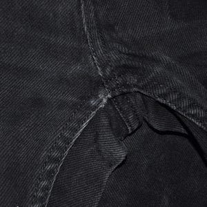 May include: Close-up of black denim fabric, showing the texture and stitching details. The image highlights the seams and construction of the garment, with a focus on the durable material and craftsmanship.