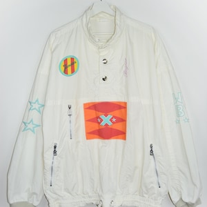 May include: White windbreaker jacket with a colorful geometric design on the front. The jacket has a high collar, a snap closure, and two zippered pockets on the sides. The jacket also features a small patch with the word "Jamaica" on the left chest.