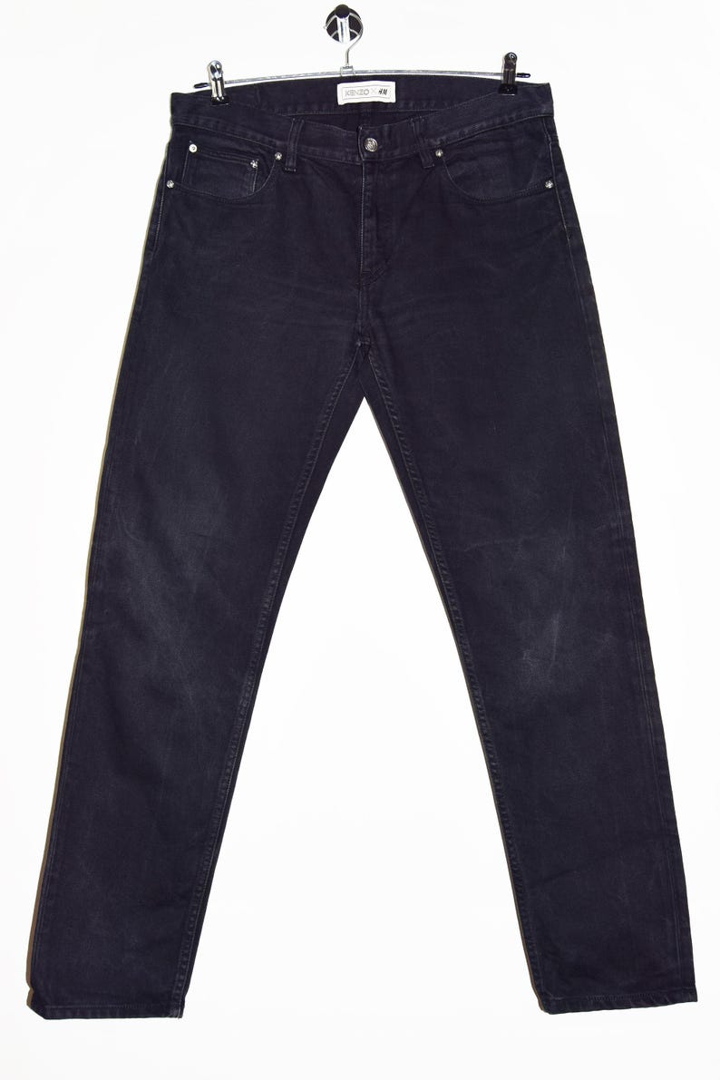 May include: Dark wash denim jeans hanging on a metal hanger. The jeans have a classic five-pocket design, a button and zipper closure, and a straight leg fit. The denim appears to be pre-worn, with some fading and wear marks.