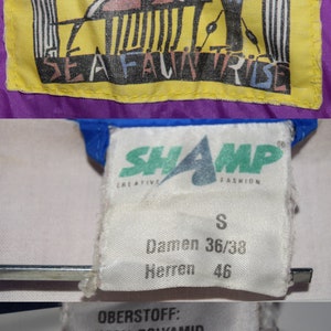 May include: A white label with black text that reads "SHAMP CREATIVE FASHION" and "S Damen 36/38 Herren 46". A yellow label with a black and blue fish design and the text "SEAFALWNTIRIBE". A white label with black text that reads "OBERSTOFF: 100% POLYAMID (wasserabweisend) FUTTER: 100% BAUMWOLLE".