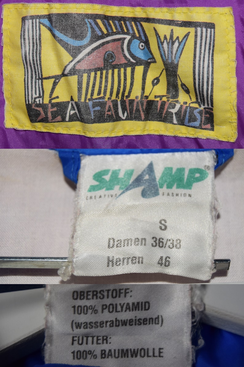 May include: A white label with black text that reads "SHAMP CREATIVE FASHION" and "S Damen 36/38 Herren 46". A yellow label with a black and blue fish design and the text "SEAFALWNTIRIBE". A white label with black text that reads "OBERSTOFF: 100% POLYAMID (wasserabweisend) FUTTER: 100% BAUMWOLLE".