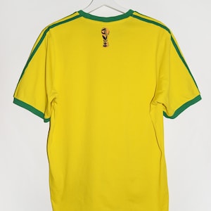 May include: Yellow short-sleeved t-shirt with green trim around the collar and sleeves. The shirt has a small graphic of a soccer trophy on the back.