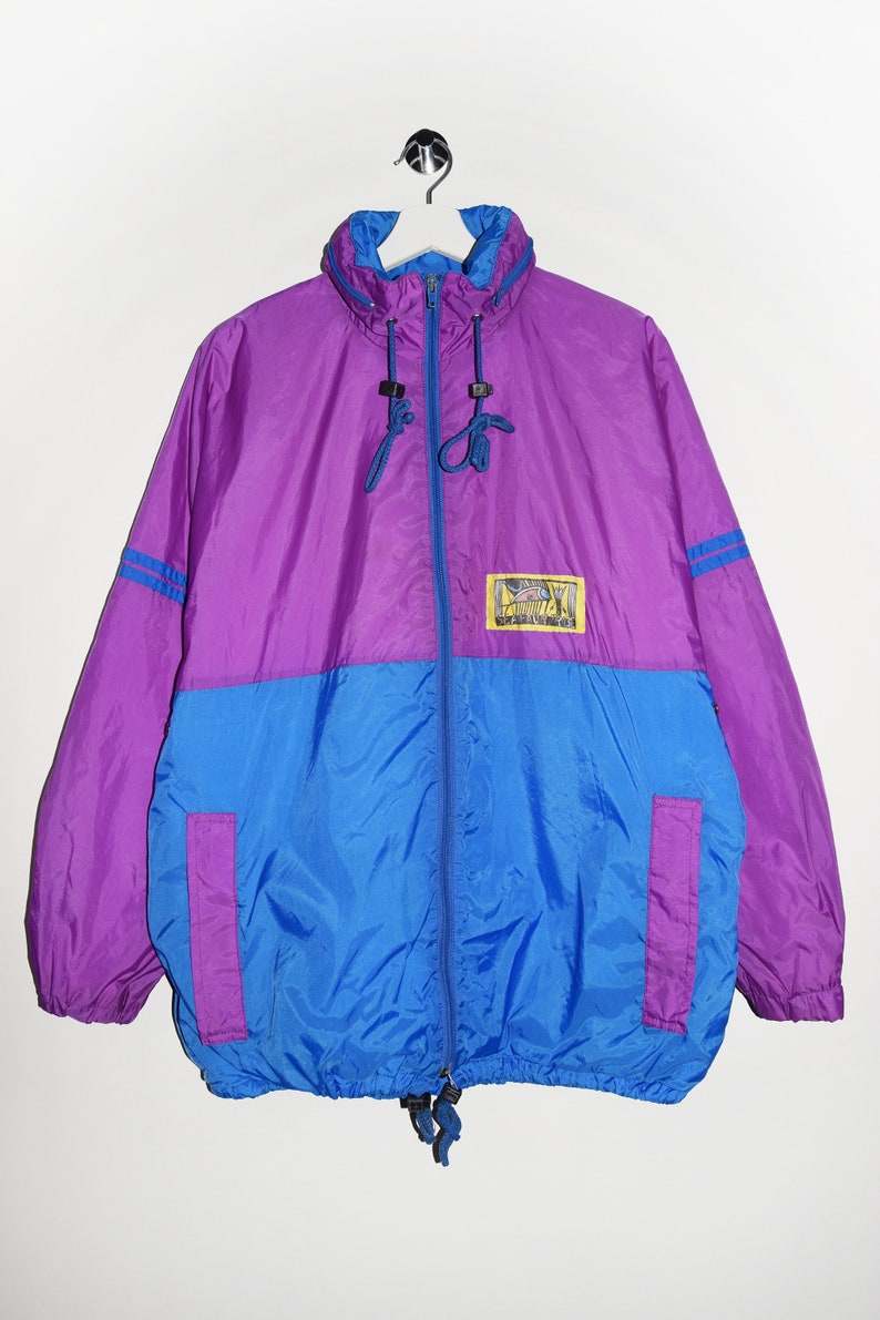 May include: A purple and blue nylon jacket with a zip fastening and a small logo patch on the front. The jacket has a drawstring hood and two pockets.