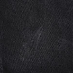 May include: Close-up of black denim fabric. The image shows the texture of the denim, with visible diagonal twill lines. The fabric appears to be a solid black color, with subtle variations in tone. The stitching is visible along the edge of the fabric.