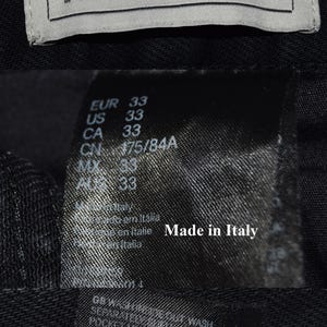 May include: Close-up of clothing tags. The top tag reads "KENZO X H.M" in black text on a white background. Below, a tag shows size information: EUR 33, US 33, CA 33. The tag also says "Made in Italy".