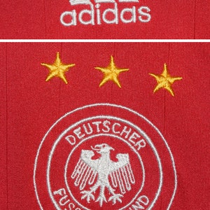 May include: Red soccer jersey with the Adidas logo, three gold stars, and the German national team crest, which reads "Deutscher Fussball-Bund".