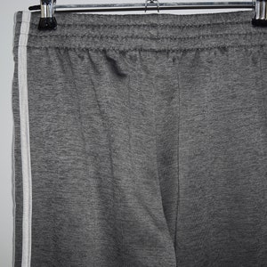 Puede incluir: Pantalones de ch&aacute;ndal grises con rayas blancas a los lados. Los pantalones de ch&aacute;ndal tienen una cintura el&aacute;stica.
