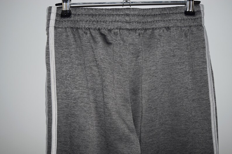 Puede incluir: Pantalones de ch&aacute;ndal grises con rayas blancas a los lados. Los pantalones de ch&aacute;ndal tienen una cintura el&aacute;stica.
