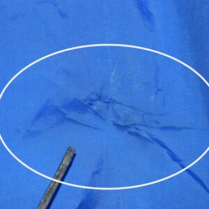 May include: Close-up of a blue fabric with a white circle highlighting a tear in the fabric.