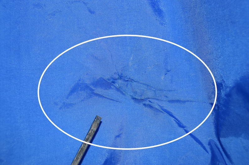 May include: Close-up of a blue fabric with a white circle highlighting a tear in the fabric.