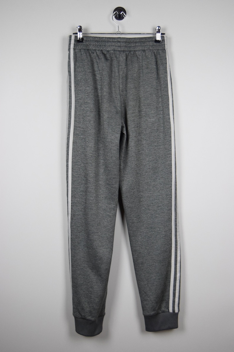 Puede incluir: Pantal&oacute;n de ch&aacute;ndal gris con rayas blancas a los lados. El pantal&oacute;n de ch&aacute;ndal tiene una cintura con cord&oacute;n y un dobladillo en la parte inferior.