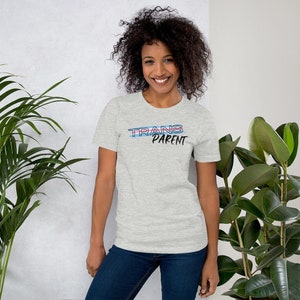 May include: A person wearing a heather grey t-shirt with the text "TRANS PARENT" in blue and pink lettering.