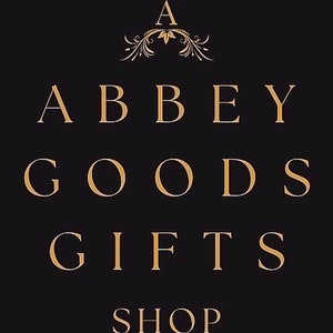 May include: Black background with gold text that reads "ABBEY GOODS GIFTS SHOP". The word "A" is at the top with a crown above it. The text is in a serif font.