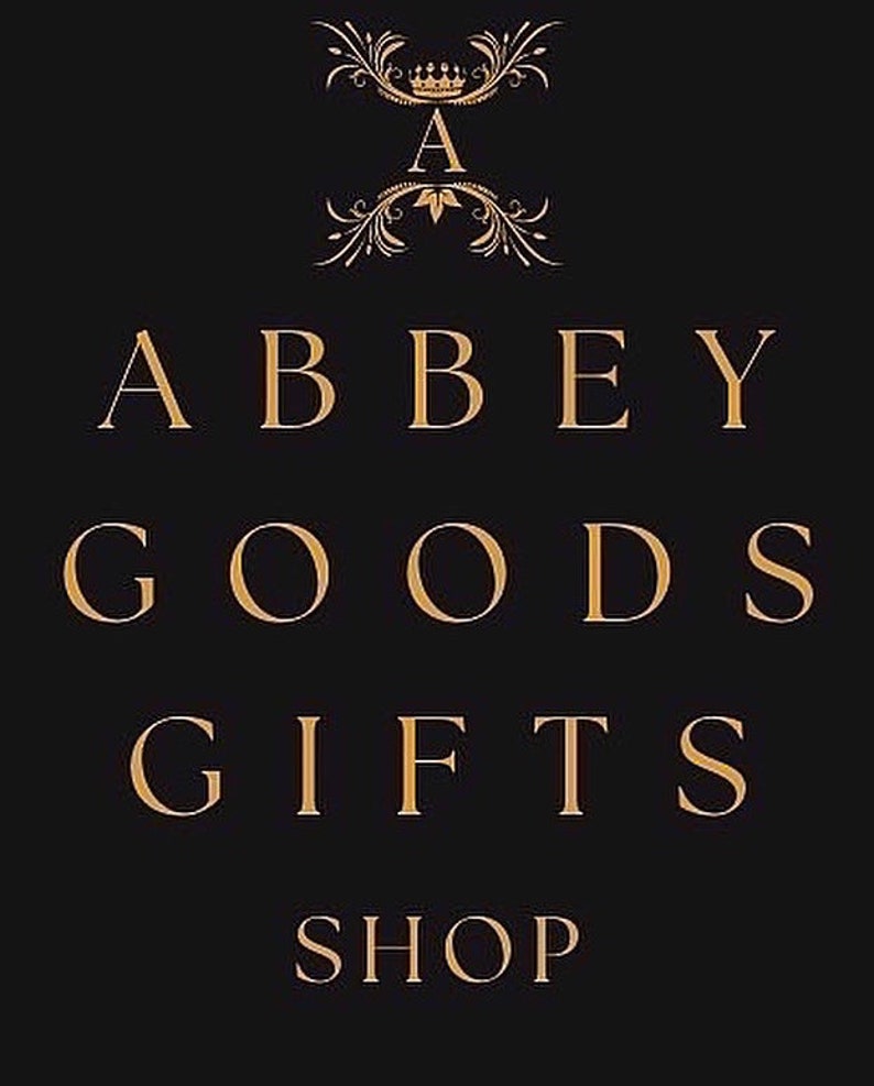 May include: Black background with gold text that reads "ABBEY GOODS GIFTS SHOP". The word "A" is at the top with a crown above it. The text is in a serif font.