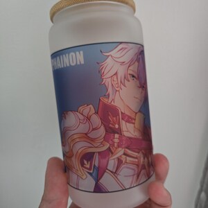Op de afbeelding: Matglazen beker met een bamboe deksel. De beker heeft een kleurrijke anime-stijl illustratie van een personage met wit haar en een rood en gouden outfit. Het woord "PHAINON" staat op de beker.