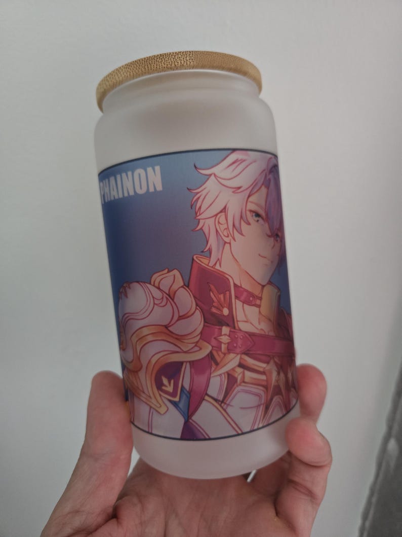 Op de afbeelding: Matglazen beker met een bamboe deksel. De beker heeft een kleurrijke anime-stijl illustratie van een personage met wit haar en een rood en gouden outfit. Het woord "PHAINON" staat op de beker.