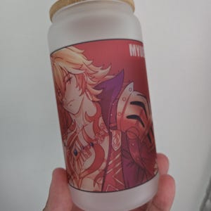 Op de afbeelding: Matte glazen beker in de vorm van een blikje met een bamboe deksel. De beker heeft een rode afbeelding van een anime-achtig personage met blond haar en een harnas. Het woord "MY" is zichtbaar aan de zijkant. Een stijlvol en uniek drankartikel.