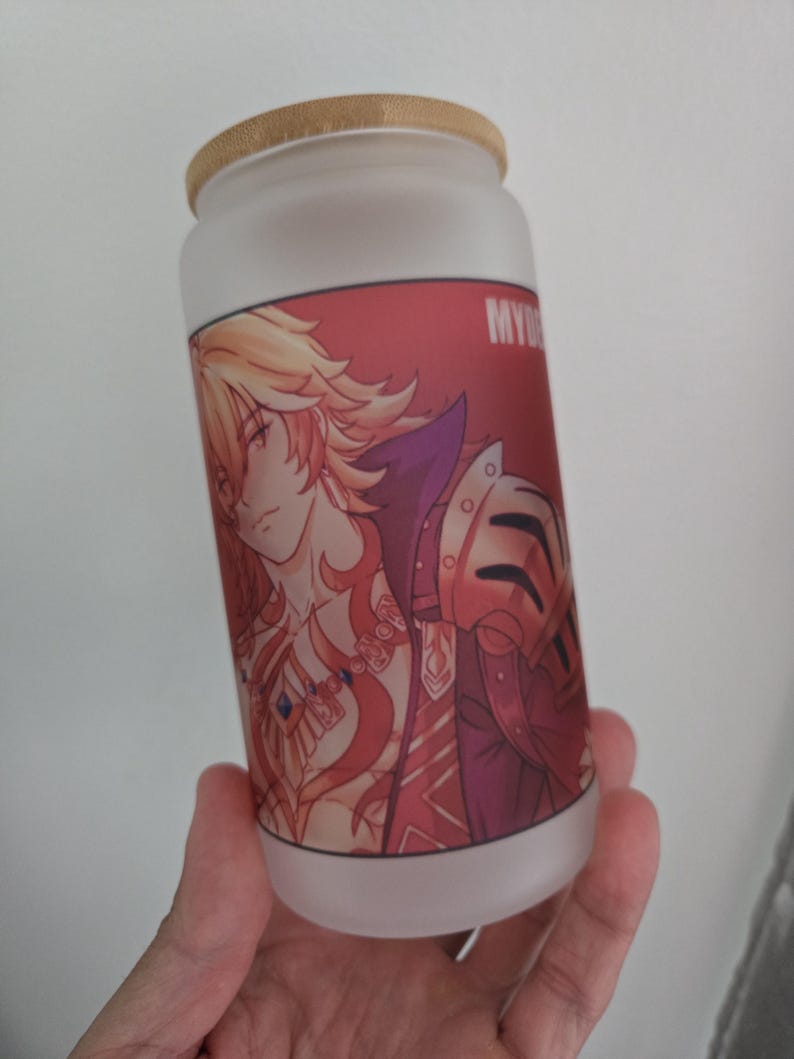Op de afbeelding: Matte glazen beker in de vorm van een blikje met een bamboe deksel. De beker heeft een rode afbeelding van een anime-achtig personage met blond haar en een harnas. Het woord "MY" is zichtbaar aan de zijkant. Een stijlvol en uniek drankartikel.