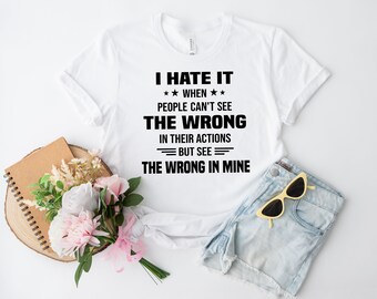 Puede incluir: Una camiseta blanca de manga corta con el texto impreso en negro: I HATE IT WHEN PEOPLE CAN'T SEE THE WRONG IN THEIR ACTIONS BUT SEE THE WRONG IN MINE. La camiseta se muestra junto a un ramo de flores rosas y blancas y unas gafas amarillas.