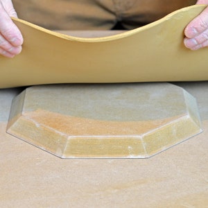 May include: A light brown ceramic plate with an octagonal shape. The plate has a slightly raised edge and a smooth surface.