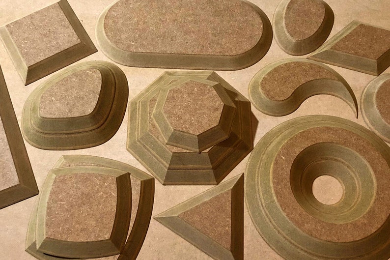 May include: A set of 10 wooden geometric shapes, each with a layered design. The shapes are in various sizes and include a square, oval, circle, diamond, and more. The shapes are made of a light brown wood with a natural finish.