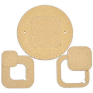 Op de afbeelding: Drie onafgewerkte houten stukken voor een knutselproject. De stukken zijn een cirkel met een vierkante uitsparing, een vierkant met een kleinere vierkante uitsparing en een kleiner vierkant.