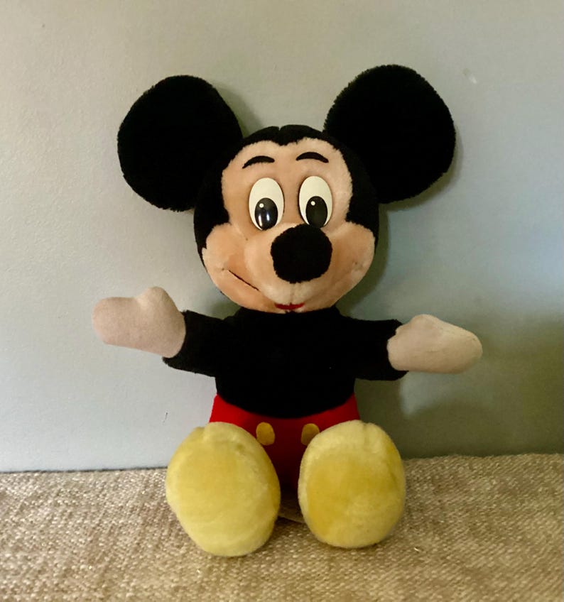 May include: A vintage plush Mickey Mouse toy with black fur, large ears, and a red and yellow outfit. The toy has a friendly expression with big eyes and a wide smile.