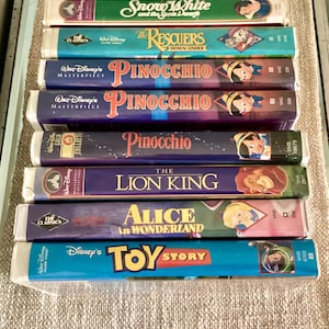 May include: A collection of eight Walt Disney VHS tapes stacked vertically. Titles include Snow White and the Seven Dwarfs, The Rescuers Down Under, three copies of Pinocchio, The Lion King, Alice in Wonderland, and Toy Story, all with colorful spines.