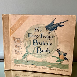 May include: The cover of a vintage children's book titled "The Funny Froggy Bubble Book" with illustrations of a frog, a crow, and a bubble. The book is written by Ralph Mayhew & Burger Johnson and illustrated by Ruth King.