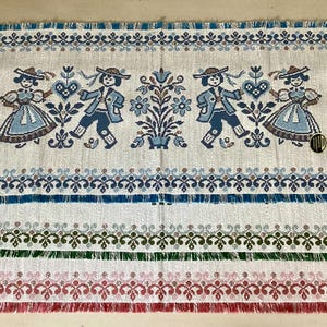 May include: Rectangular woven placemats with a folk art design. The top mat features a repeating pattern of dancing figures in blue and brown, with a blue and white border. Additional mats in green and red are visible.