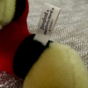 May include: A yellow, black, and red plush toy with a white tag that reads "Disneyland&reg; Walt Disney World&reg; &copy; DISNEY&reg;".