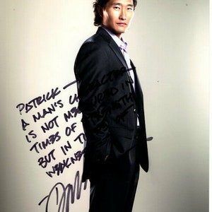 May include: A man in a black suit and a light purple shirt, standing against a white background. He is looking at the camera and has a serious expression on his face. The text "PATRICK - A MAN'S CHARACTER IS NOT MATURED IN TIMES OF STRENGTH BUT IN TIMES OF WEAKNESS" is written in black marker on the white background.