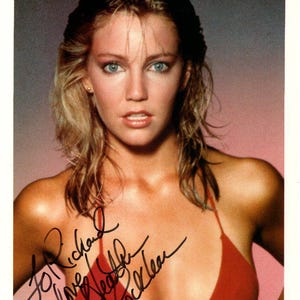 Puede incluir: Un retrato de cerca de una mujer con el pelo largo y rubio que lleva un top de bikini rojo. La mujer sonríe y mira a la cámara. La imagen está firmada "To Richard Love Heather Locklear".