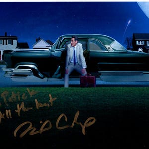May include: A black and green vintage car with a man in a suit standing next to it. The car is parked in front of a house with a starry night sky in the background. The image is signed "To Patrick, All the best, Rip Off."