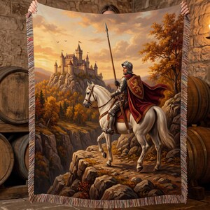 May include: A woven throw blanket featuring a detailed illustration of a knight in silver armor riding a white horse, holding a long spear, and wearing a red cape with a gold lion emblem, set against a backdrop of a castle on a mountain.