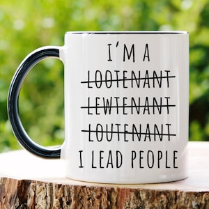 May include: White ceramic mug with a black handle and rim. The mug has black text that reads "I'm a Loote-nant Lewtenant Loutenant I lead people". The text has lines through the incorrect spellings of "lieutenant".