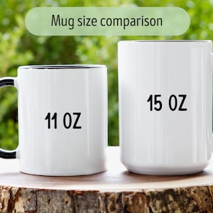 Op de afbeelding: Zij-aan-zij vergelijking van twee witte keramische mokken met zwarte randen en handvatten. De mok aan de linkerkant is 11 oz en de mok aan de rechterkant is 15 oz.