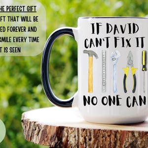 Op de afbeelding: Een witte keramische mok met een zwart handvat. De mok heeft een zwarte afbeelding met de tekst "Als David het niet kan repareren, kan niemand het" met een tekening van gereedschap, waaronder een hamer, een liniaal, een moersleutel, een tang en een schroevendraaier.