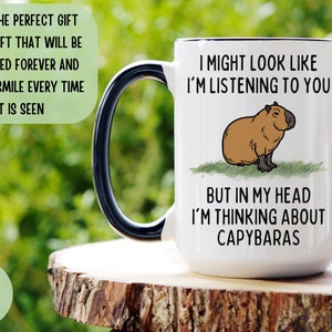 Peut inclure: Mug en c&eacute;ramique blanche avec une anse et un bord noirs, orn&eacute; d'une illustration de capybara et du texte "I might look like I'm listening to you, but in my head I'm thinking about capybaras." Le mug contient environ 444 ml.