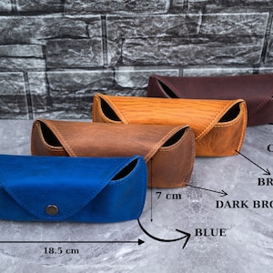 May include: Four leather eyeglass cases in blue, brown, dark brown, and cherry. The blue case is 7 cm high and 18.5 cm long. Each case features a snap closure and a curved design.