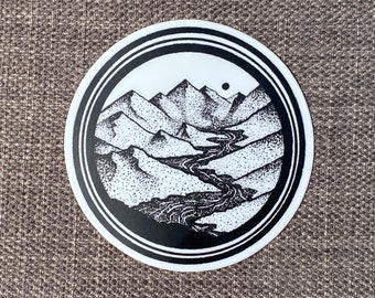 May include: Black and white sticker with a circular design featuring a stylized mountain range and a river winding through it. The mountains are dotted with small white dots, creating a textured effect.