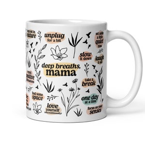 May include: White ceramic mug with black and beige botanical illustrations and phrases like "deep breaths, mama" and "one day at a time." The mug features a curved handle and is designed for hot beverages.
