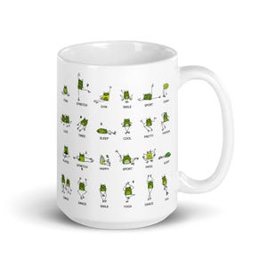 May include: White ceramic mug featuring green frog illustrations in various yoga poses, with words like "Yoga", "Stretch", and "Smile". The mug has a curved handle and a glossy finish.