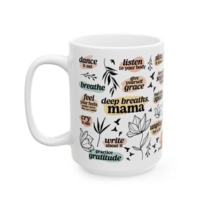 May include: White ceramic mug with black and teal text and illustrations. The mug features phrases like "breathe," "listen to your body," and "deep breaths, mama." Floral and bird illustrations are also included.