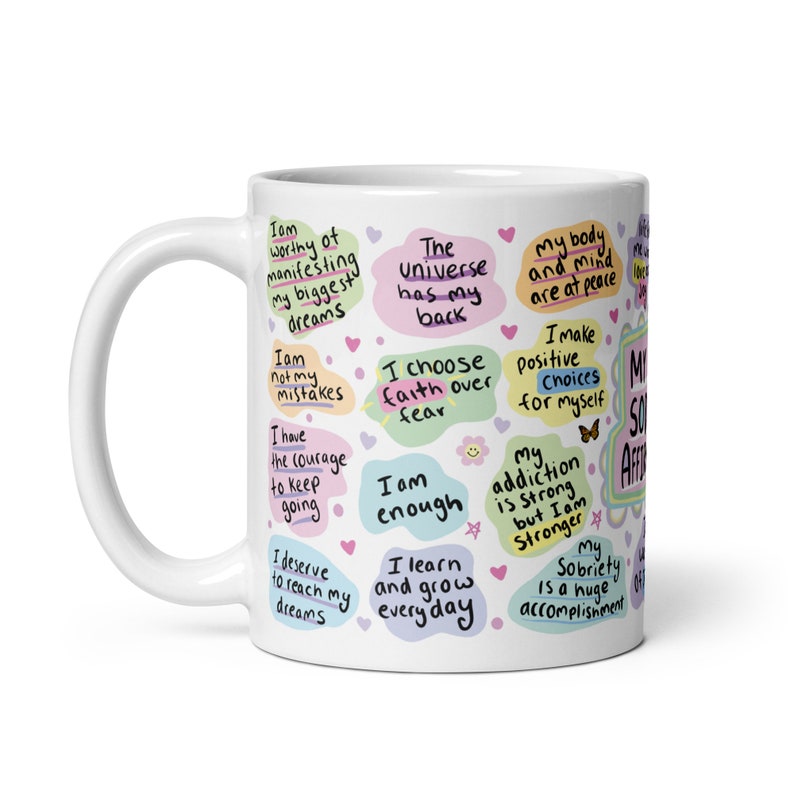 May include: White ceramic mug with colourful text and illustrations. The text includes positive affirmations such as "I am worthy of manifesting my biggest dreams", "I choose faith over fear", "I am enough", and "My sobriety is a huge accomplishment".