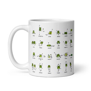 May include: White ceramic mug featuring a whimsical design of green frogs in various yoga poses. The mug has the words "YOGA", "STRETCH", "GYM", "SMILE", "SPORT", "LOVE", "TIRED", "SLEEP", "COOL", "PRETTY", "PLATES", "HAPPY", "FROG", and "DANCE".
