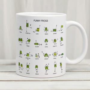 May include: White ceramic mug featuring the text "FUNNY FROGS" and illustrations of green frogs in various yoga and exercise poses. The mug has a white handle and is suitable for hot or cold beverages.