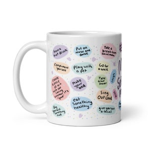Peut inclure: Une tasse en c&eacute;ramique blanche avec un motif color&eacute; comportant des phrases comme "prendre une boisson chaude", "se complimenter", "jouer avec un animal de compagnie", "faire son lit", "manger quelque chose de sain", "faire une pause des m&eacute;dias sociaux", "aller se promener", "prendre une douche chaude", "chanter &agrave; tue-t&ecirc;te", "se faire un soin du visage", "rire" et "sourire".